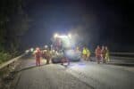 Roadworkers in orange and yellow high-vis clothing laying new surface on M11 motorway under lights of heavy machinery.