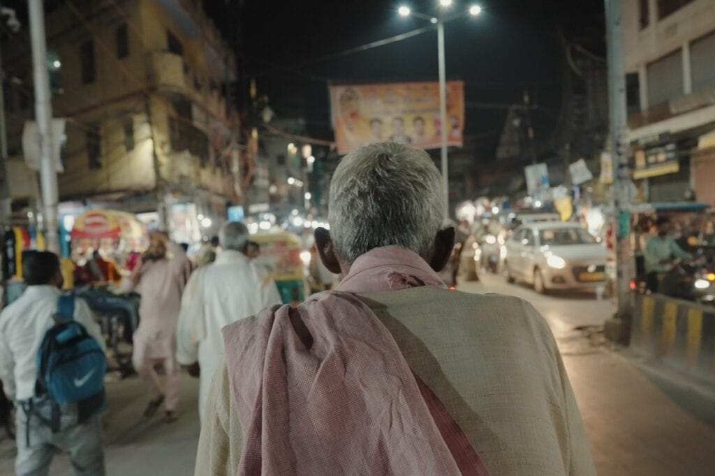 Back on elderly man's head as he walks through busy city street at night.