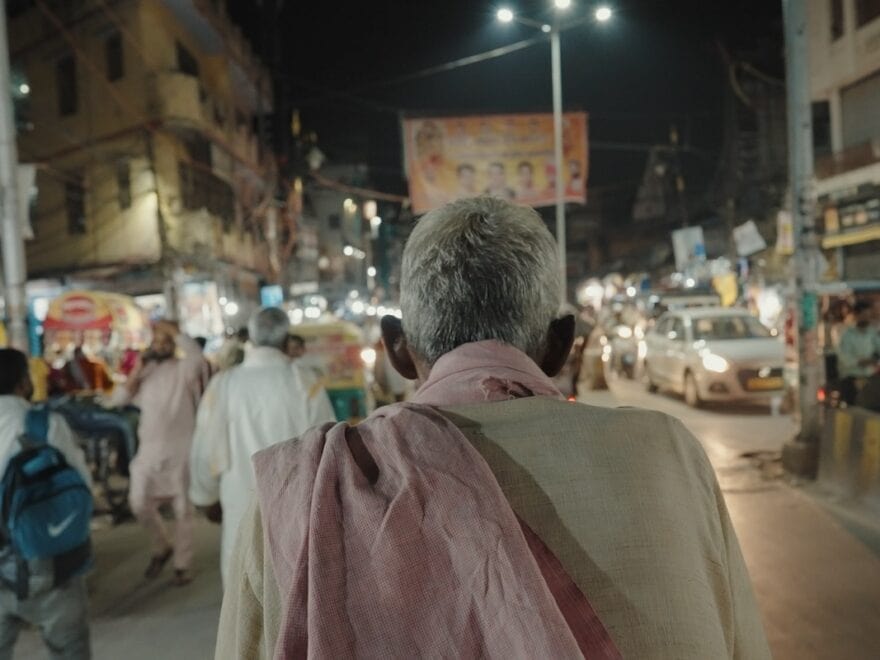 Back on elderly man's head as he walks through busy city street at night.