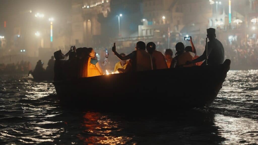 Group of people, some holding camera phones, in what looks like tourist boat on Ganges River at night.