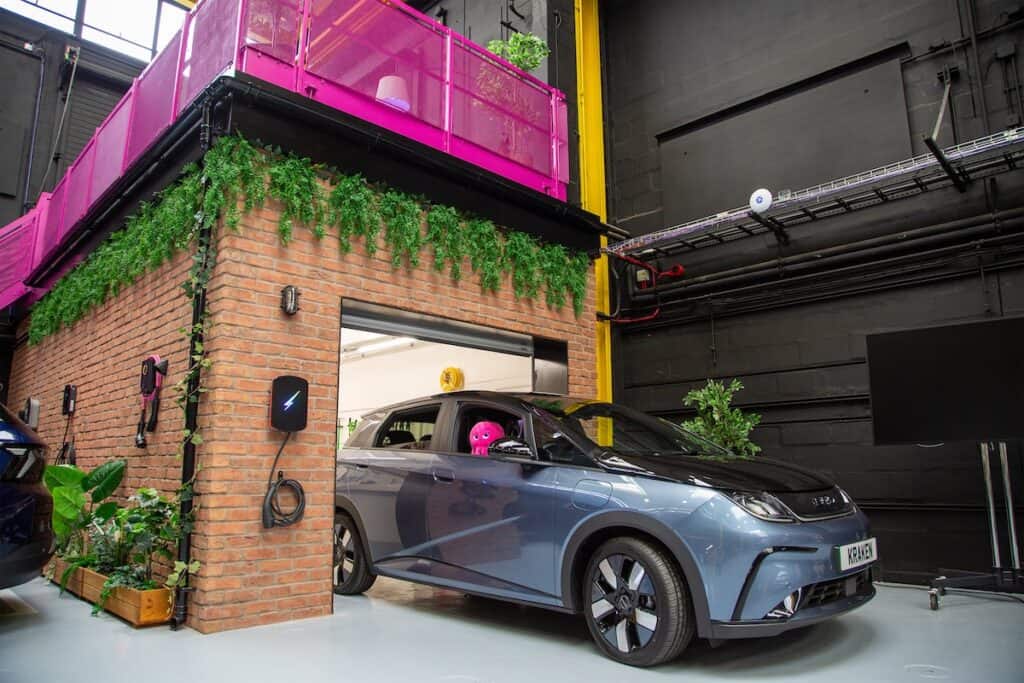 Electric vehicle (with pink Octopus brand soft toy in driver's window) seen emerging from brick garage structure within office building.