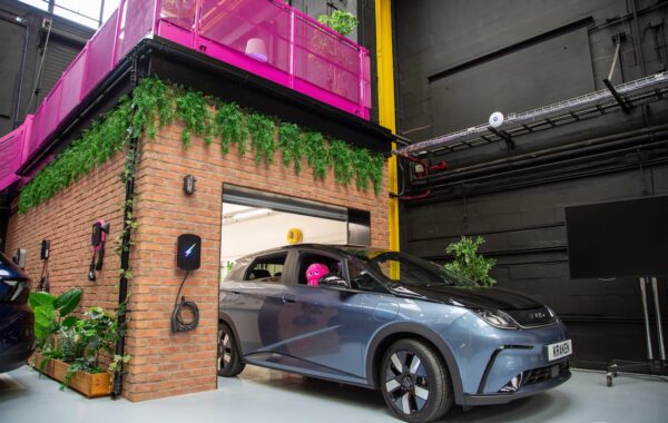 Electric vehicle (with pink Octopus brand soft toy in driver's window) seen emerging from brick garage structure within office building.