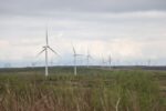 Established wind farm in open fields and moorland, on a grey day with clouds overhead.