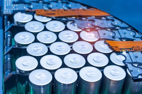 Close-up of lithium-ion battery pack module, revealing grid of upright chrome-coloured cylinder-shaped batteries, sat within blue and orange casing.