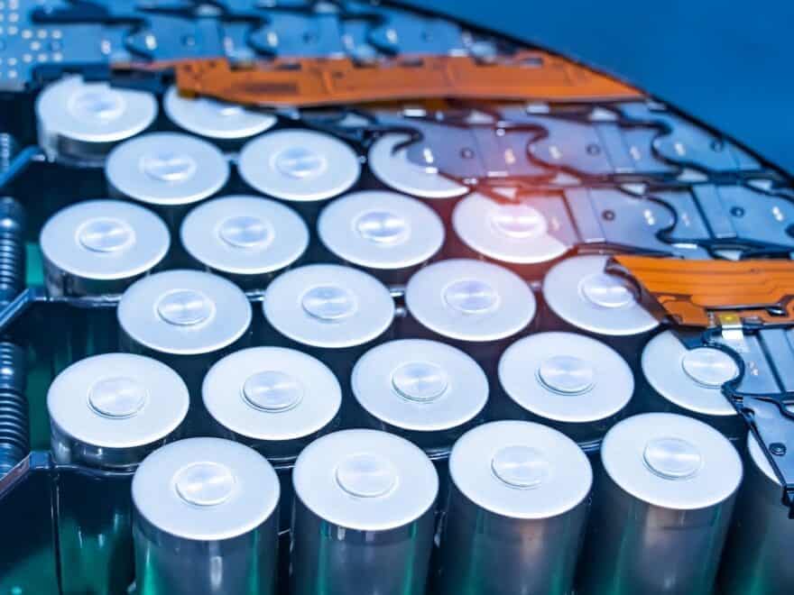 Close-up of lithium-ion battery pack module, revealing grid of upright chrome-coloured cylinder-shaped batteries, sat within blue and orange casing.