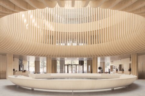 Exposed ribbed wooden structure creates circular atrium feature above equally large ring-shaped furniture piece in lobby area.