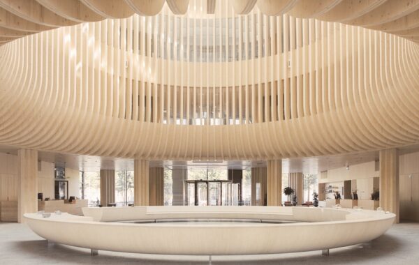 Exposed ribbed wooden structure creates circular atrium feature above equally large ring-shaped furniture piece in lobby area.