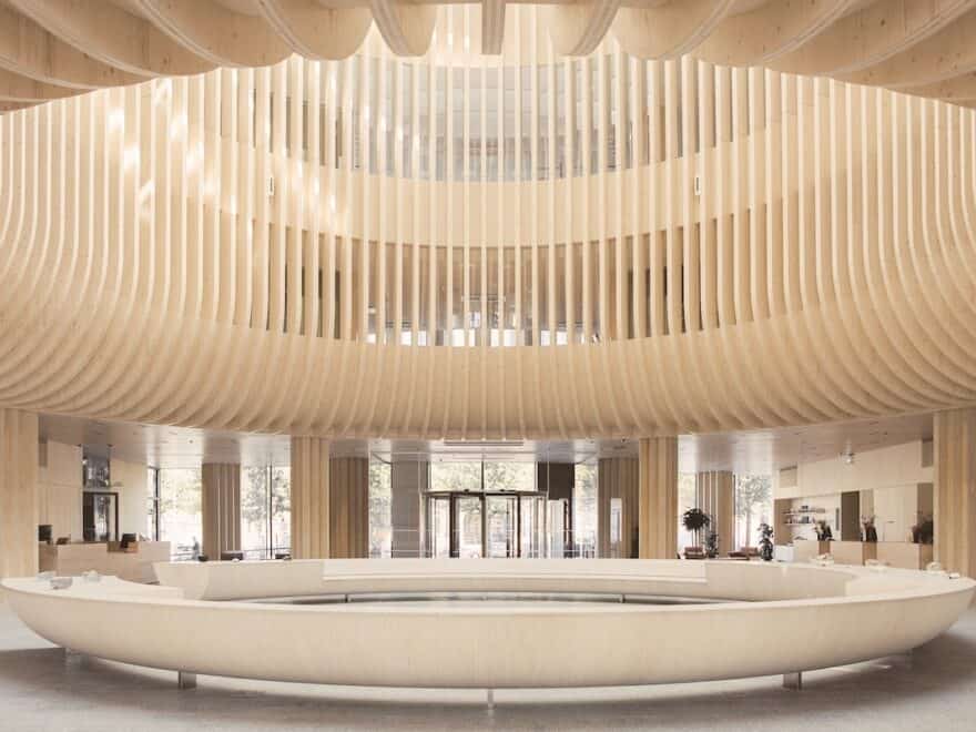 Exposed ribbed wooden structure creates circular atrium feature above equally large ring-shaped furniture piece in lobby area.