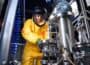 Person in bright yellow HAZMAT suit, complete with face mask, works on pilot test manufacturing equipment.