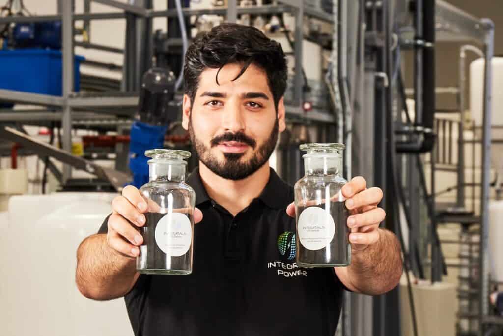 Behnam Hormozi, Founder & CEO of Integrals Power, holding two jars of black granular materials up to camera, with company branding on labels.