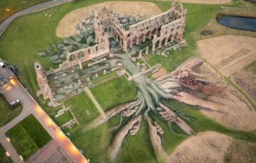 Aerial view of land art installation in and around ruins of Whitby Abbey, with hands drawn holding roots of tree in natural earth greens and browns.