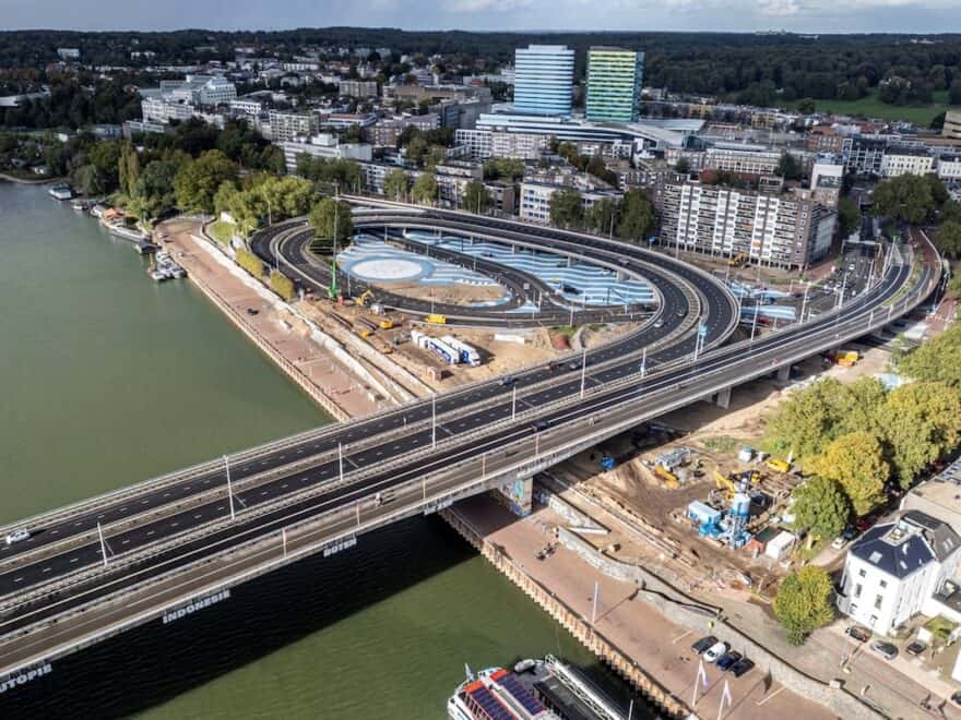 Aerial view of works to bank or river in Arnhem, with road bridge running across, plus blue and white skate park around and under carriageway.