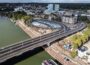 Aerial view of works to bank or river in Arnhem, with road bridge running across, plus blue and white skate park around and under carriageway.