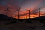 Wind farm turbines pictured in silhouette against colourful sky at sunset.