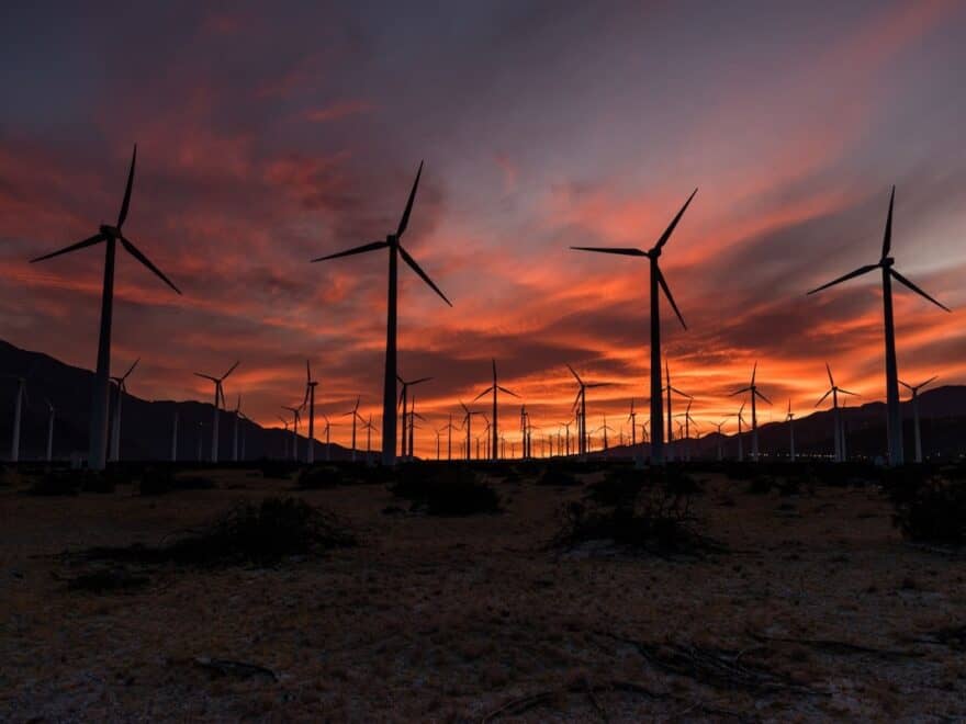 Wind farm turbines pictured in silhouette against colourful sky at sunset.