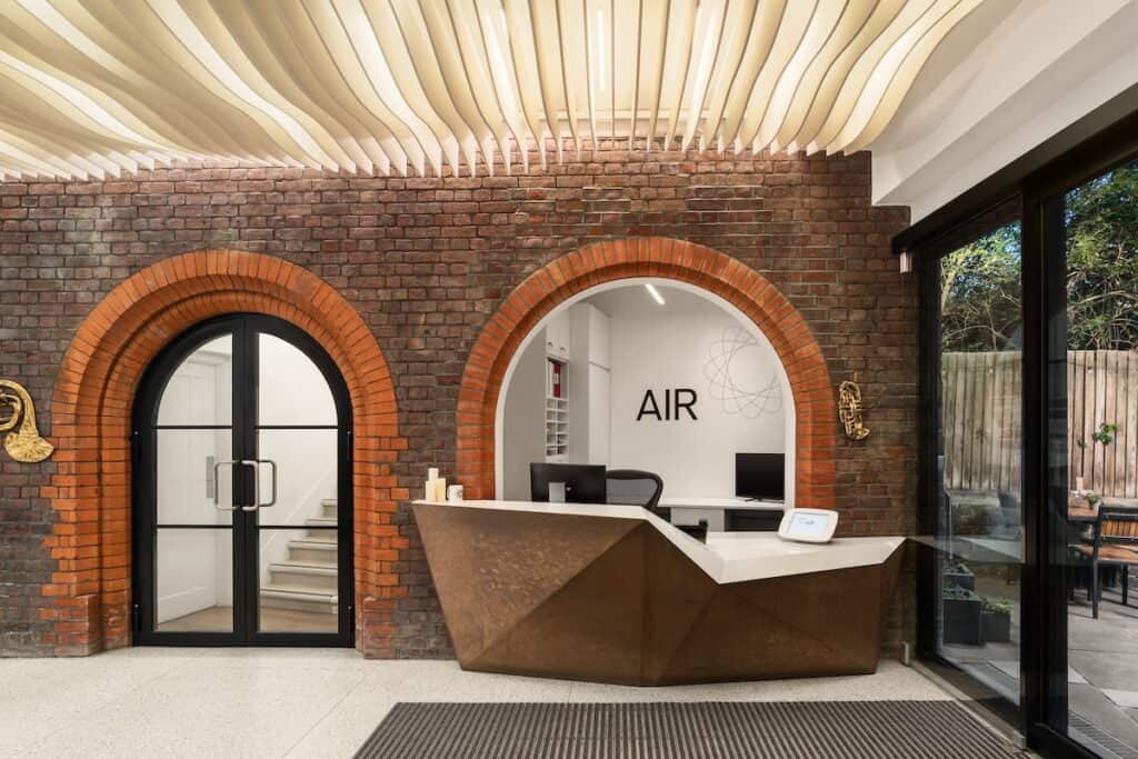 Reception desk for AIR studios, with name visible on wall behind, brick walls with arched doorway to stairs, plus sliding glass doors to exterior.