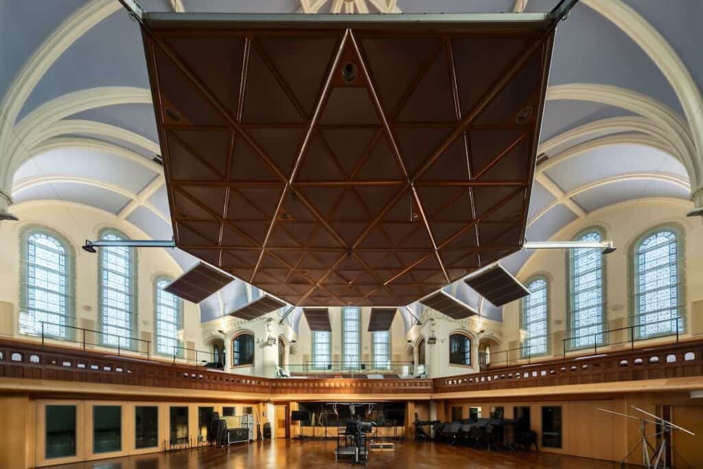 Panoramic interior of large recording and performance space with arched windows above gallery level and acoustic baffles suspended from ceiling.