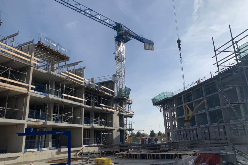 Cartesius building site, with tower crane in centre, sat between two three- to four-storey apartment blocks under construction, blue sky overhead.