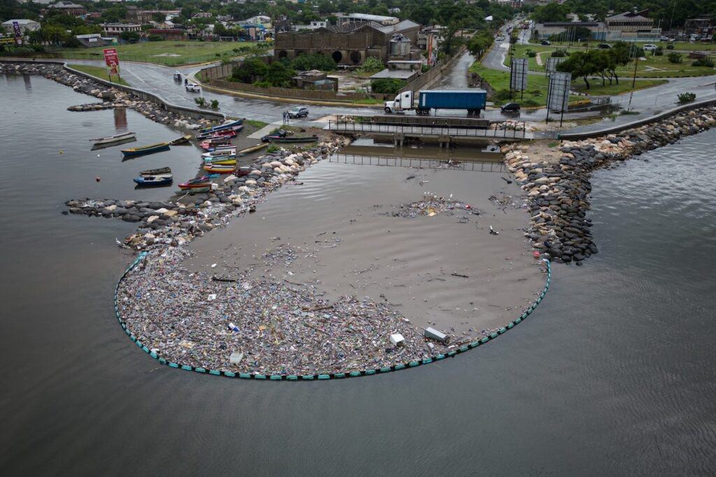 View from distance of Interceptor Barrier 009 in a loop in Kingston Harbour, and trash within near end, plus clear water and boats without.