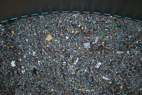 Aerial view of floating (mostly plastic) trash filling area trapped behind blue cordon of Interceptor Barrier, beyond which seawater is garbage-free.