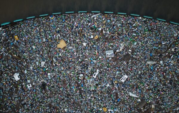 Aerial view of floating (mostly plastic) trash filling area trapped behind blue cordon of Interceptor Barrier, beyond which seawater is garbage-free.