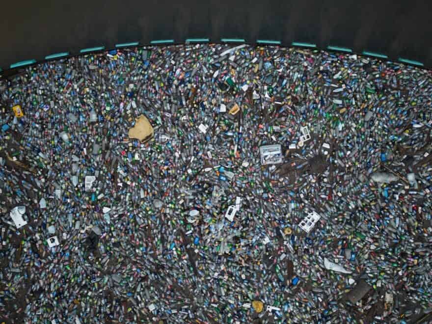 Aerial view of floating (mostly plastic) trash filling area trapped behind blue cordon of Interceptor Barrier, beyond which seawater is garbage-free.