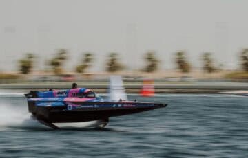 Aoki Racing Team RaceBird boat in blue and pink colours speeding in elevated mode across water, with background blurred.