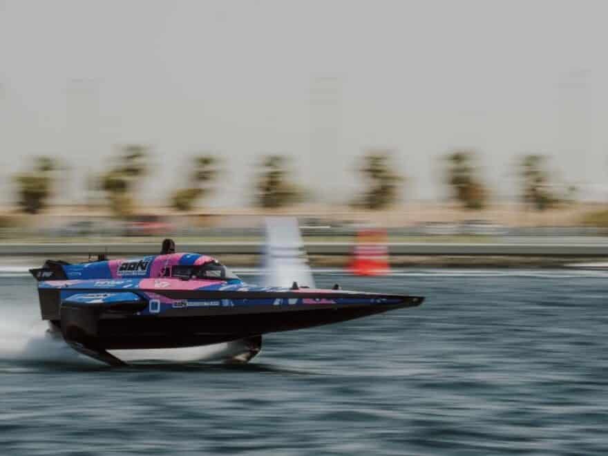 Aoki Racing Team RaceBird boat in blue and pink colours speeding in elevated mode across water, with background blurred.