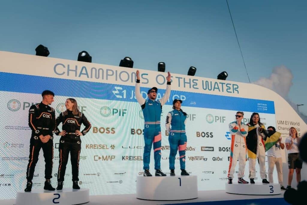 Winners podium for 'Champions of the Water', with Aoki Racing Team celebrating in centre in blue and pink colours.