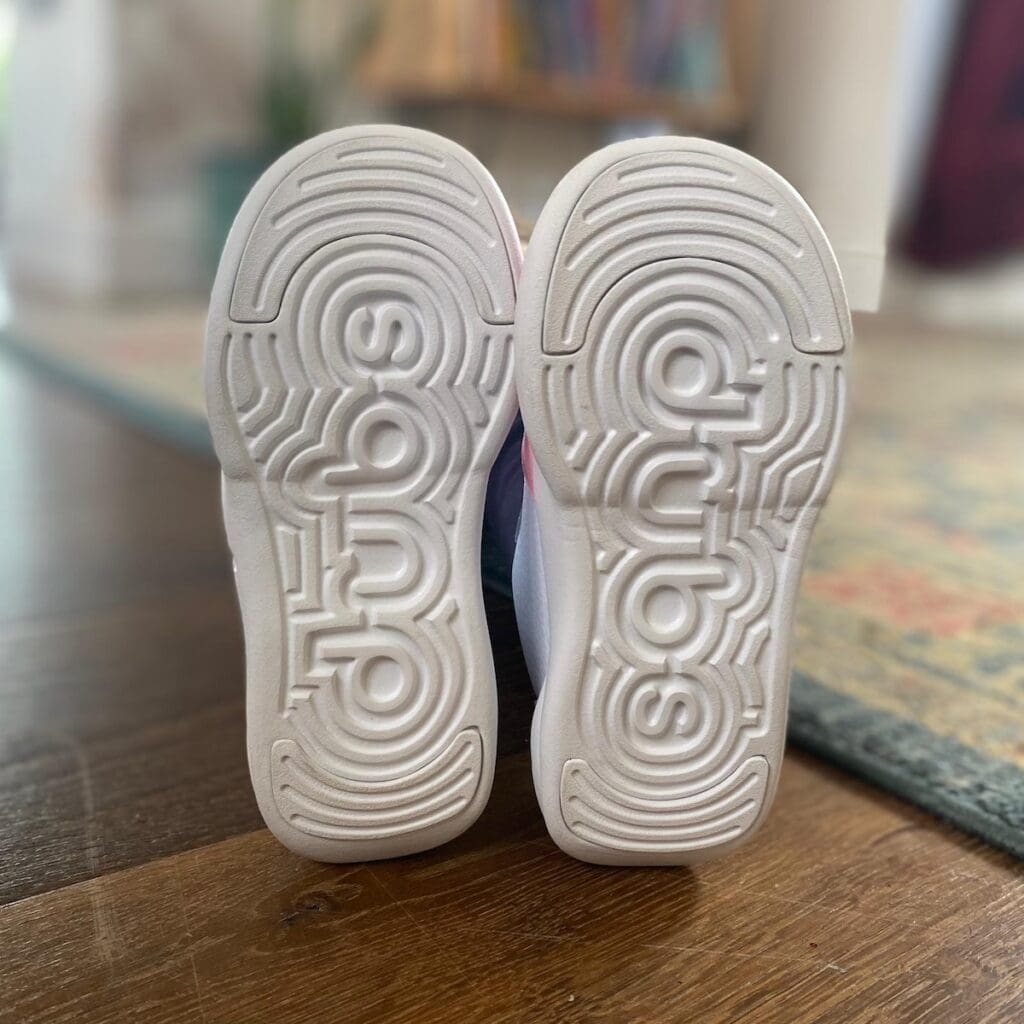 Shot of used white branded soles of Dubs footwear upright on wood floor.