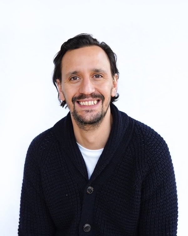 Portrait of Stuart Davis, smiling, wearing dark chunky cardigan over plain white t-shirt.