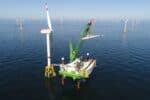 Neptune installation deck with crane shown at sea in green and white DEME livery, in position beside turbine with offshore wind farm behind.