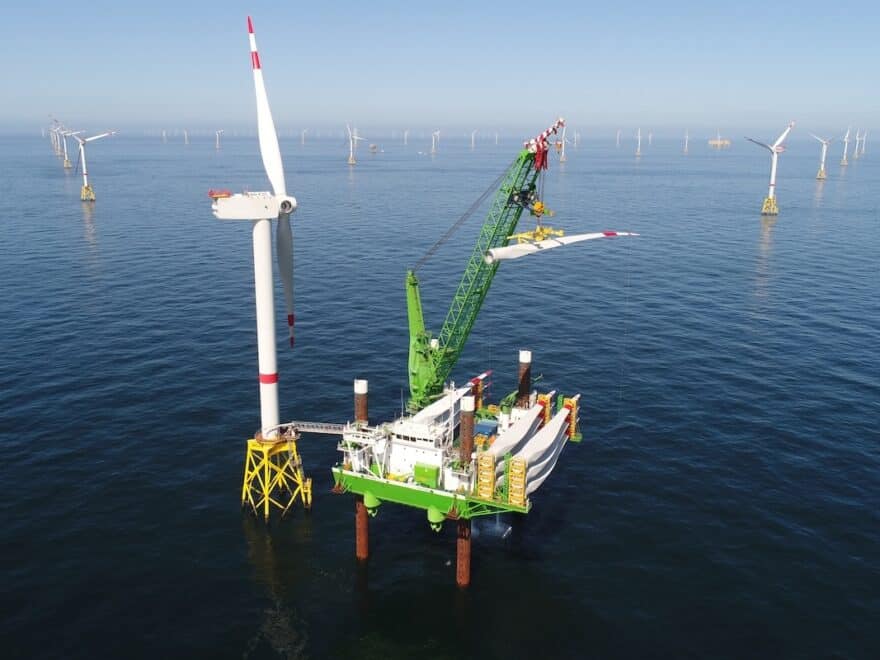 Neptune installation deck with crane shown at sea in green and white DEME livery, in position beside turbine with offshore wind farm behind.