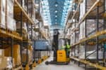 Yellow forklift blurred in action between warehouse racking loading Geopack tote box onto shelving.