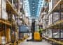 Yellow forklift blurred in action between warehouse racking loading Geopack tote box onto shelving.