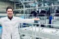 Oxwash Founder Kyle Grant pictured smiling in white workwear bearing company name, arms outstretched in front of laundry machinery.