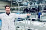 Oxwash Founder Kyle Grant pictured smiling in white workwear bearing company name, arms outstretched in front of laundry machinery.