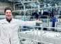 Oxwash Founder Kyle Grant pictured smiling in white workwear bearing company name, arms outstretched in front of laundry machinery.