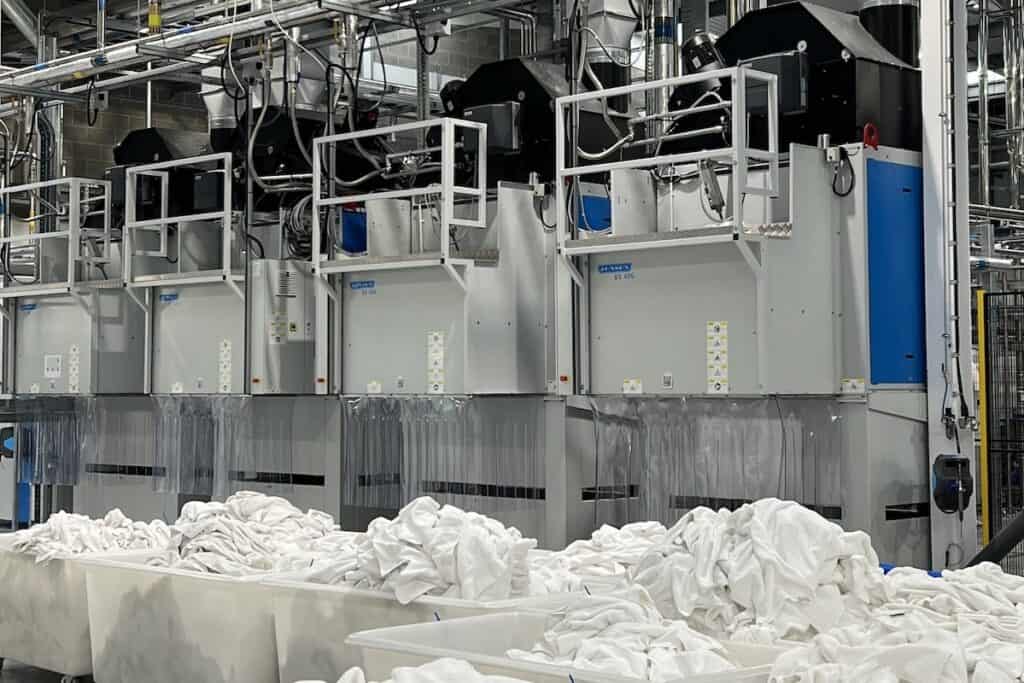 Large plastic tubs of white laundry in front of machinery, ready for washing.
