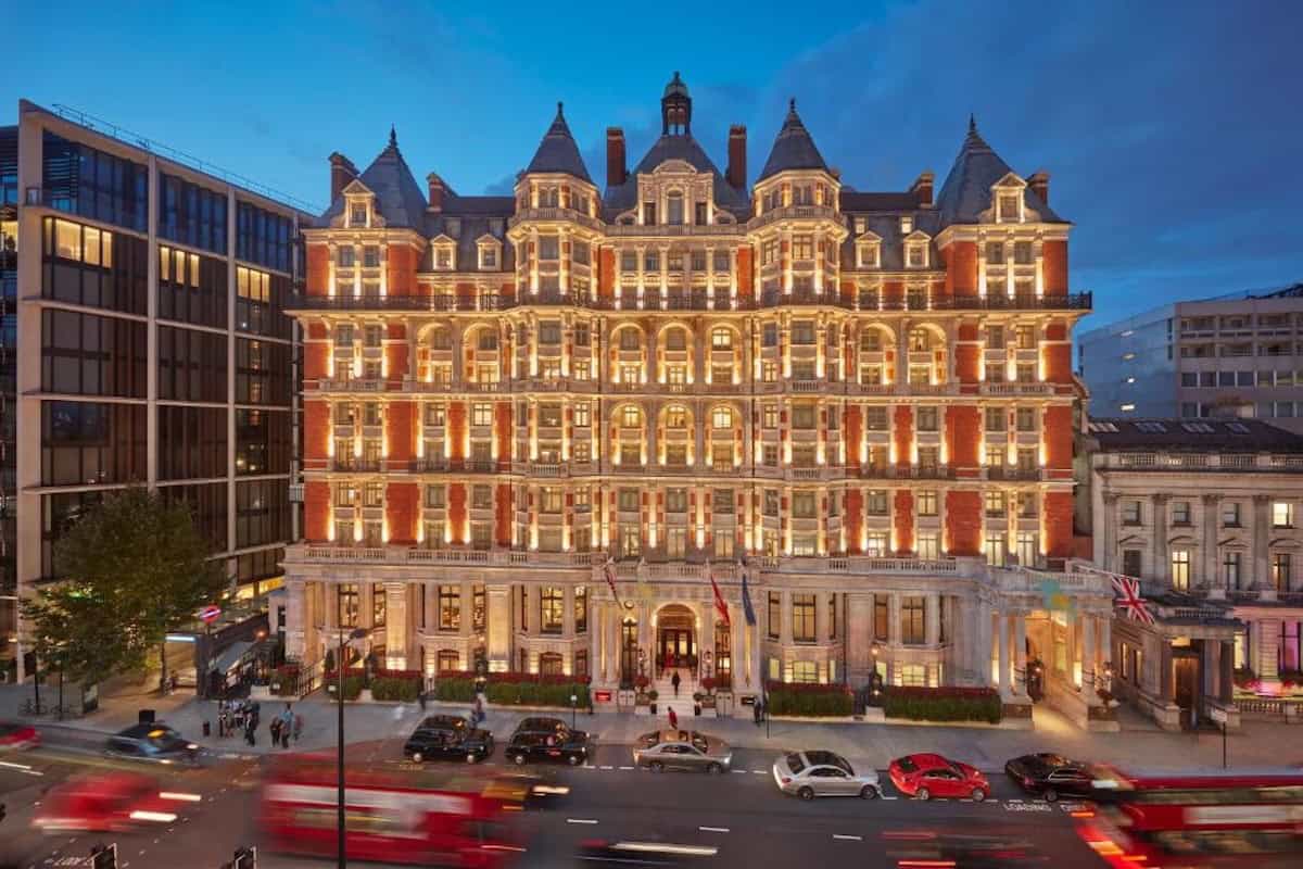 Front elevation of Mandarin Oriental Hyde Park hotel in London, illuminated at twilight, with red London bus and black cab taxis in foreground.