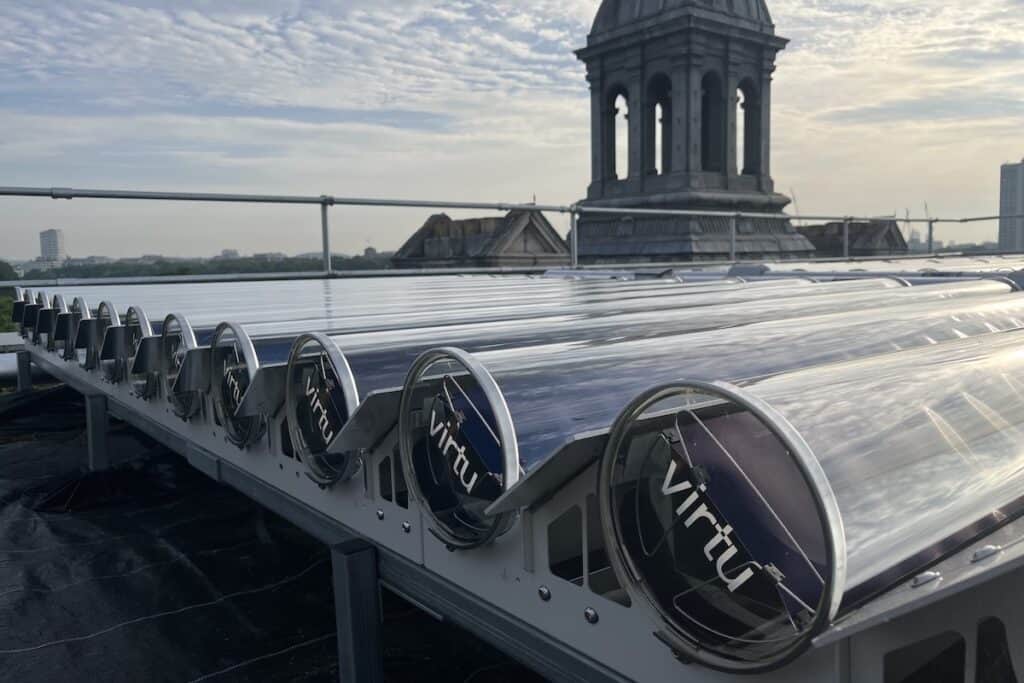 End-on close-up of rooftop solar thermal tubes, with Virtu brand name on end, plus top of architectural tower behind against evening sky.