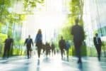 Out-of-focus image of a diverse mix of office workers in suits, walking on polished surface, glazing all around, reflecting greenery to suggest nature.