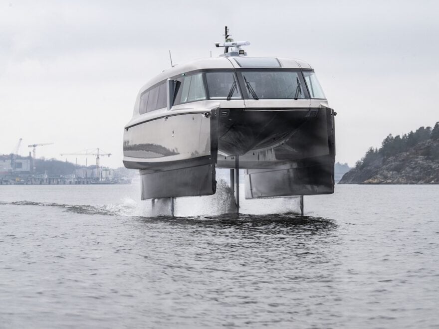 Candela P-12, the world's first electric hydrofoil ferry, pictured head-on, in full flow and up out of the water, coastline in background.