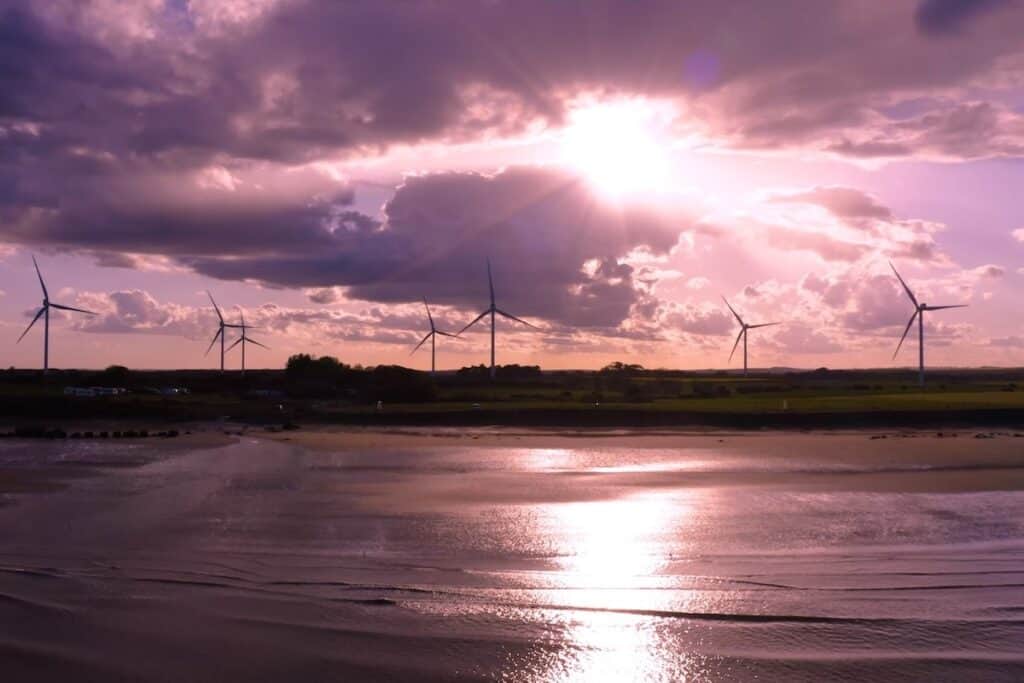 Onshore wind turbines pictured at sunset by water's edge.