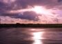 Onshore wind turbines pictured at sunset by water's edge.