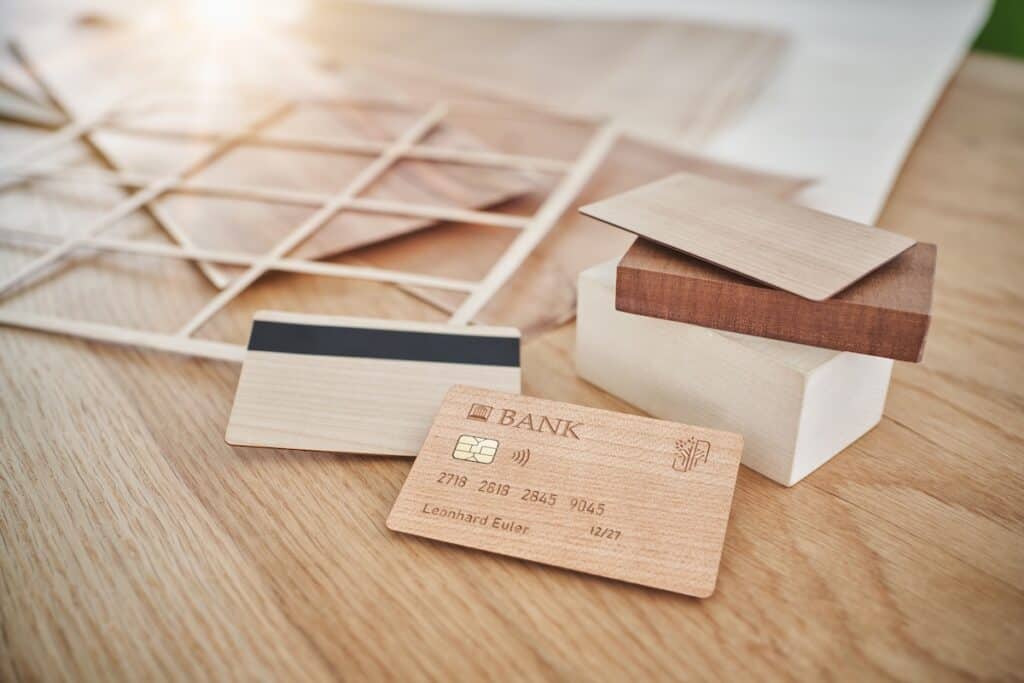 Wooden bank cards showing front and back, including chip and magnetics strip, on wood table, along with timber grid frame and blocks.