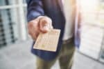 Wood COPECTO bank card in foreground, presented chip first to viewer by male hand, purple jacket, green trousers, white shirt out of focus behind.