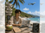 Square ChatGPT of person working at laptop at beachfront table under palm tree, destinations signpost behind; chalkboard to fore lists pros and cons; airplane overhead behind; faded duplicate 25% panels L & R.
