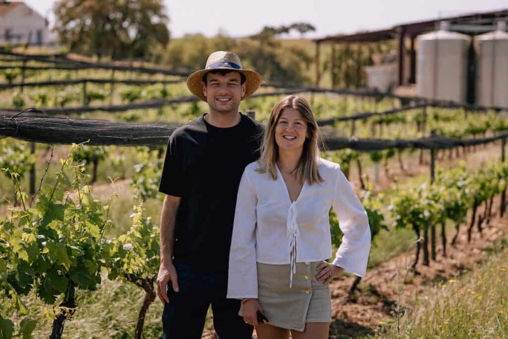 Tellia co-founders in sunny vineyard: Vincent Trastour (L) in dark t-shirt and straw hat; Coline Labadie de Faÿ (R) in white blouse and pale skirt.