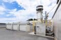 Rendering of Yanmar Rice Husk Biochar Production System with grey industrial plant alongside garage-like units in yard, blue skies behind.